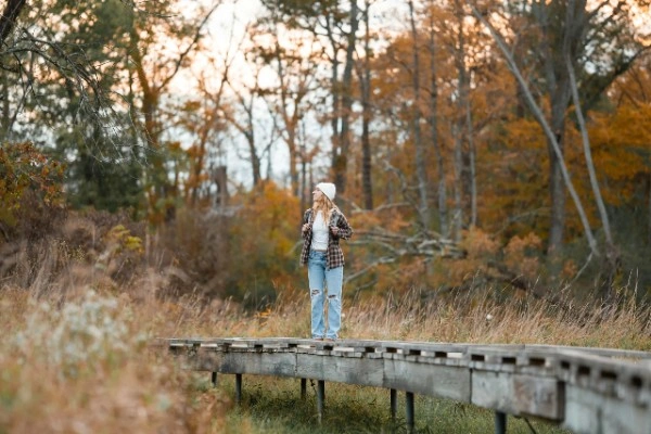 Woman standing on a wooden path in a forest, embracing solitude and reflection during autumn, symbolizing a travel mindset