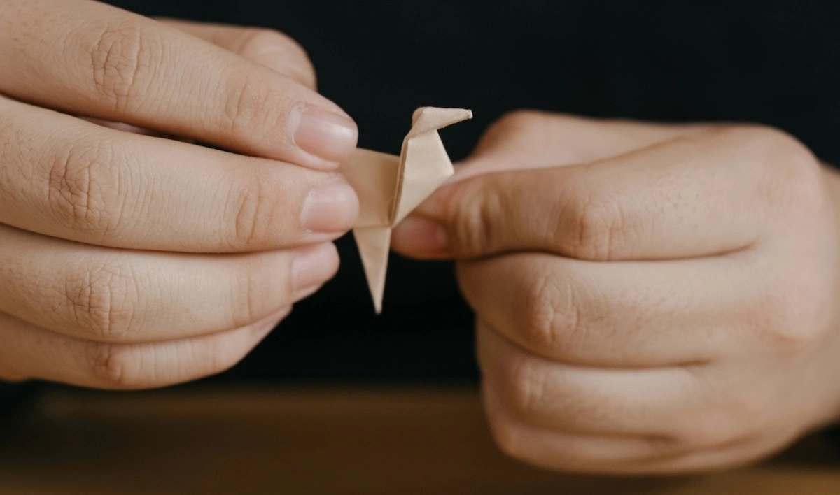 Hands carefully folding a small origami crane, demonstrating precision and focus in developing a travel-inspired craft skill
