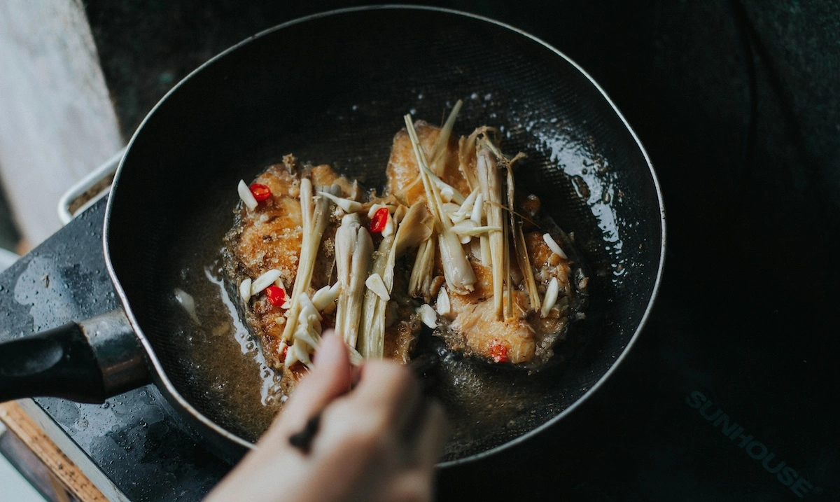 Hands adding lemongrass to sizzling shrimp and aromatics in a dark wok, recreating authentic Asian flavors at home
