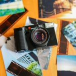 Vintage film camera surrounded by scattered travel photographs and orange film strips, creating a nostalgic collage of travel memories
